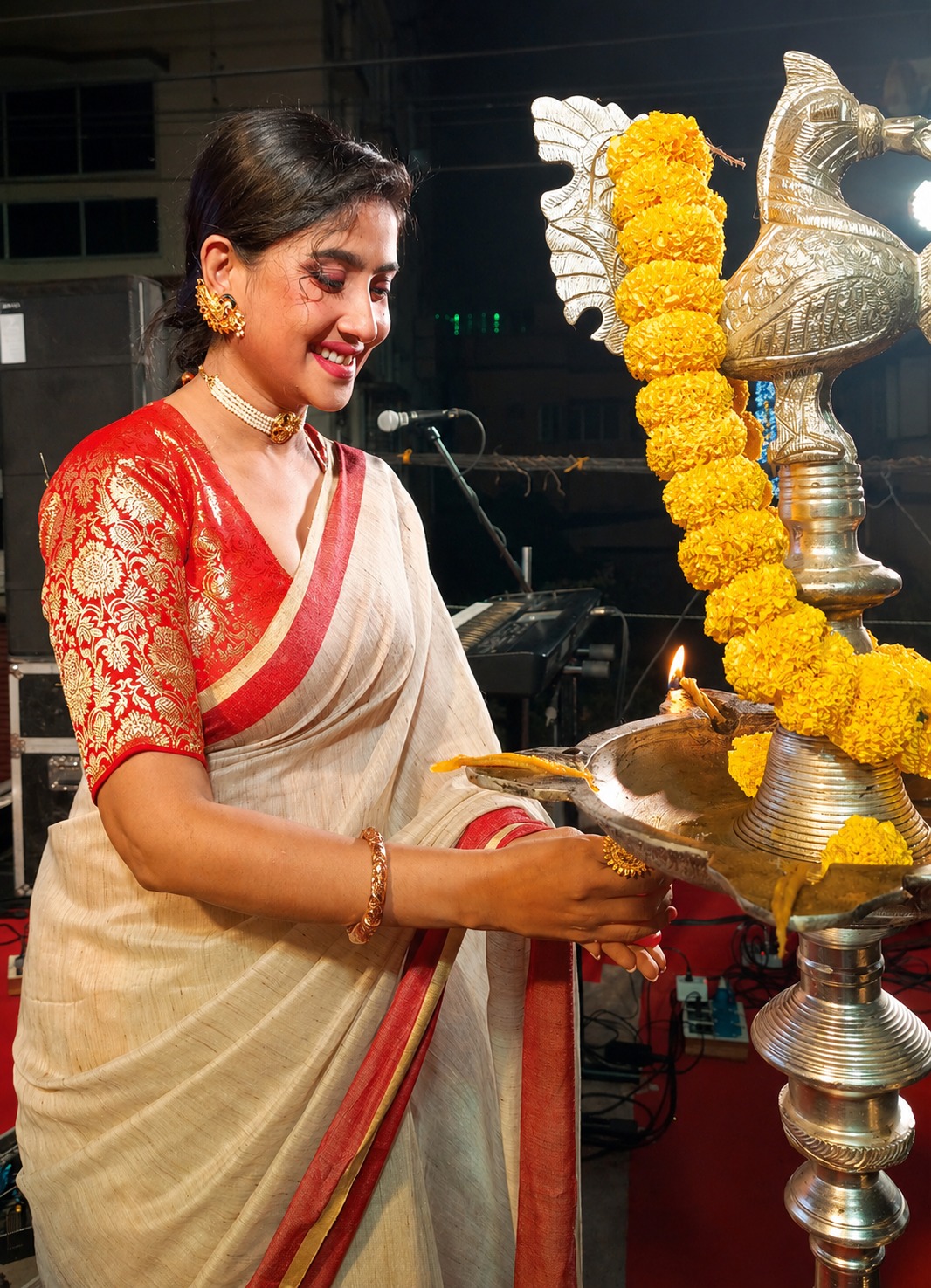 A guest in a red and cream saree lighting the ceremonial brass lamp